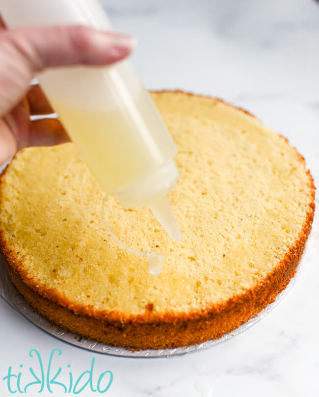 Lemon cake soak being added to a layer of vanilla cake with a squeeze bottle.