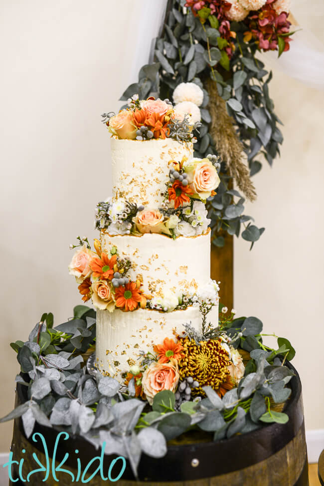 Three tier fall wedding cake frosted in Italian Meringue Buttercream, decorated with flowers and gold leaf.
