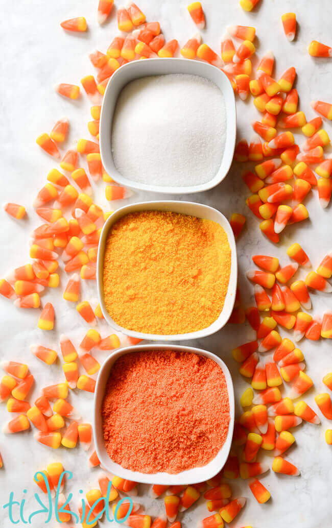 White, yellow, and orange sugar for making cotton candy, surrounded by candy corn candies.