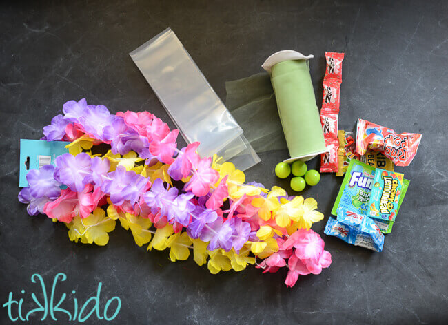 Artificial flower Hawaiian leis, plastic tubing, tulle, and candy on a black chalkboard background.