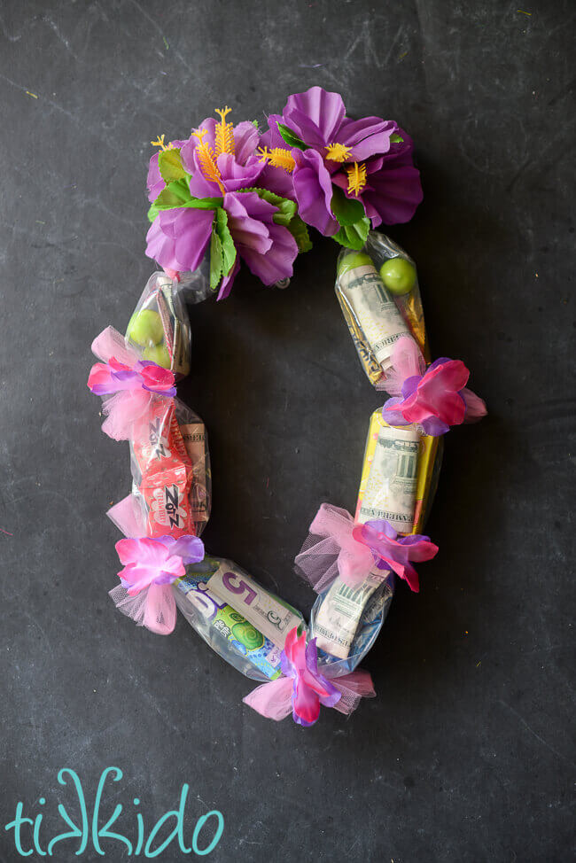 Hawaiian lei filled with candy and cash on a black chalkboard background.