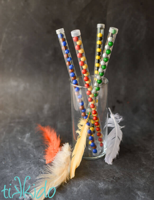 Four clear plastic candy wands filled with Hogwarts house colors chocolate candies, feather attached with black thread to the top of each wand.
