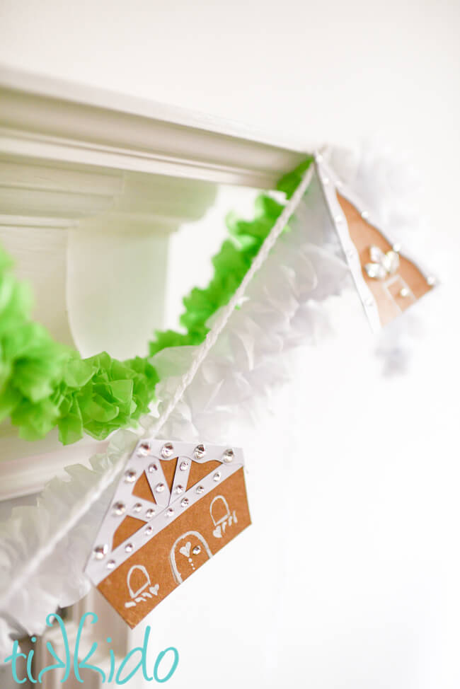 Cardboard Gingerbread house garland hanging on a fireplace mantel.