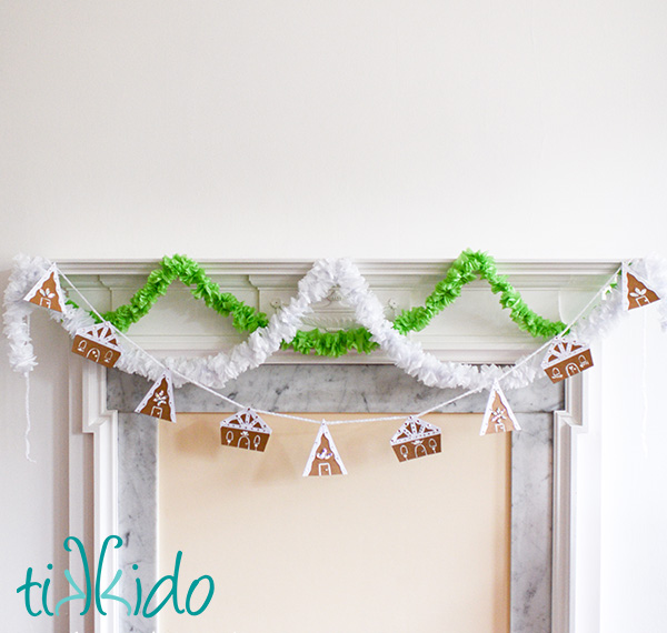 Cardboard gingerbread house garland hanging from a white fireplace mantel.