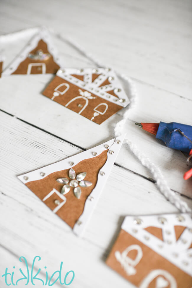 Cardboard gingerbread house garland being assembled with a glue gun.