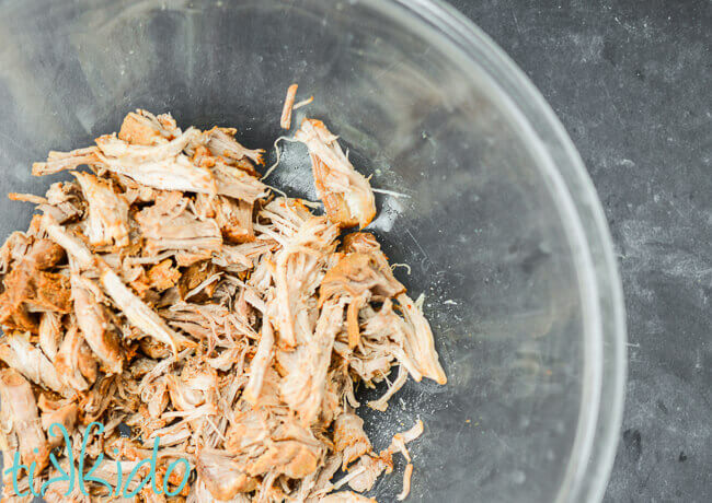 Glass bowl full of shredded pulled pork cooked with Carolina style flavorings.