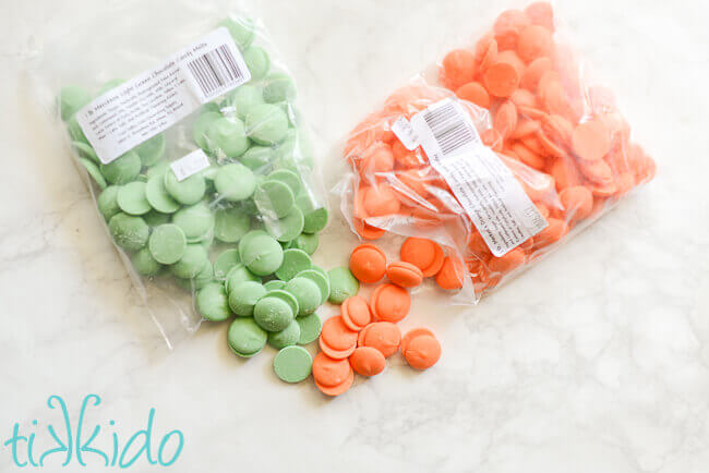 Green and orange chocolate candy melts spilling out of the bags onto a white marble surface.