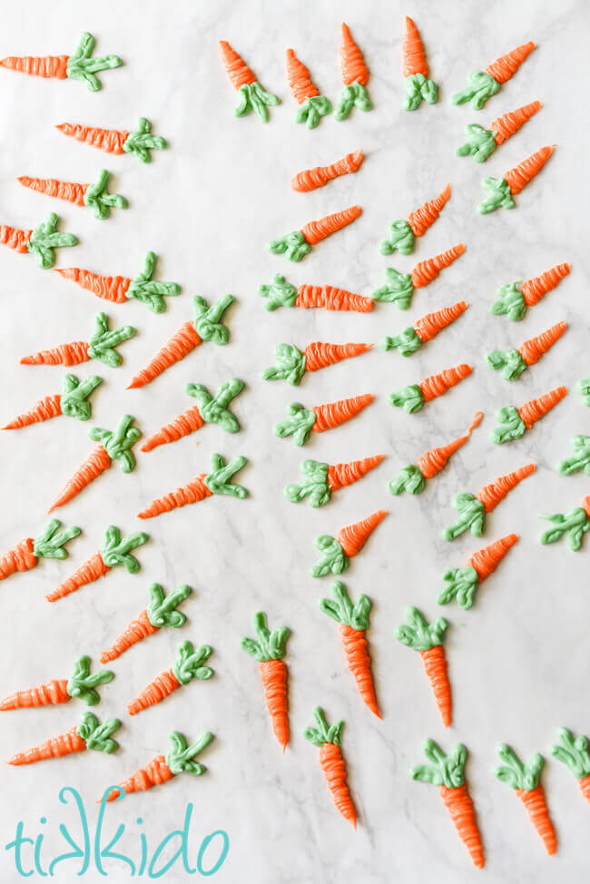 Small carrots made out of orange and green chocolate melting wafers piped into a carrot shape.  White marble background.