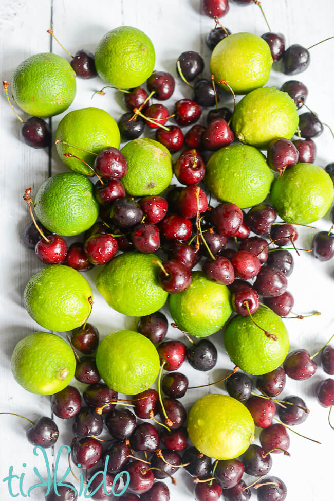 Freshly washed sweet cherries and limes piled on a white wooden surface.