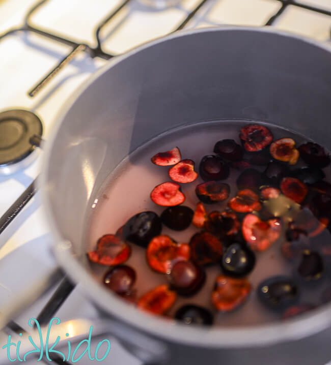 Halved and pitted cherries in a saucepan with water and sugar on the stovetop to make cherry simple syrup for cherry limeade.