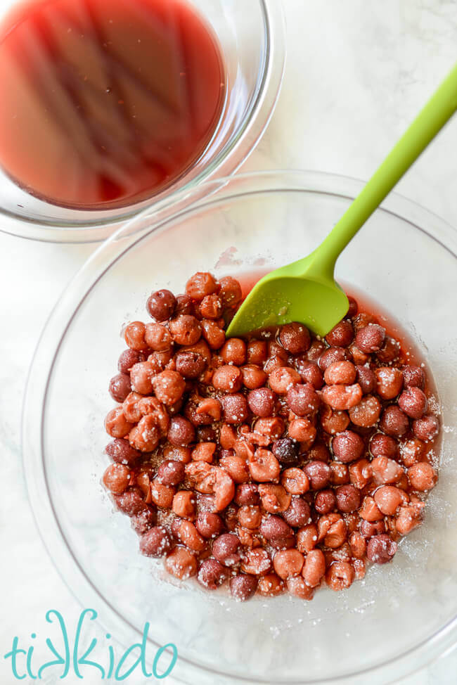 Cherry pie filling ingredients mixed together in a clear bowl with a green spatula.