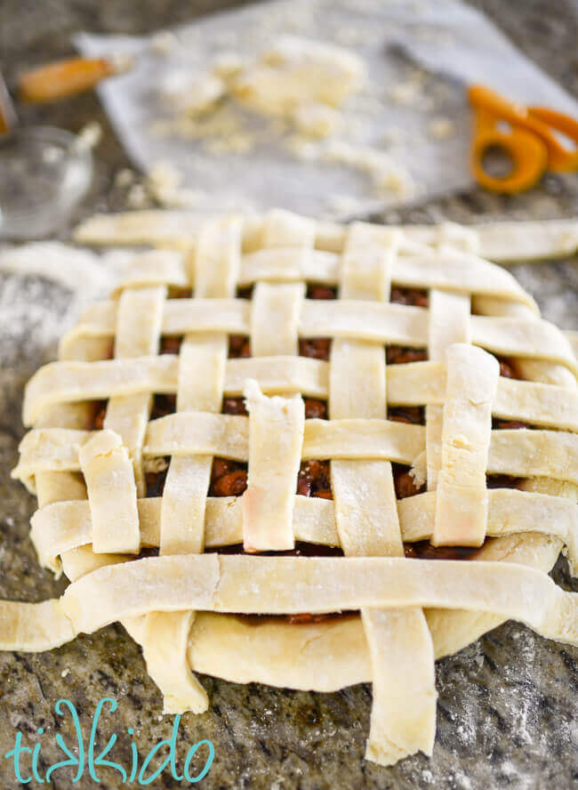 Pie crust being woven into a lattice pie crust top for a cherry pie.