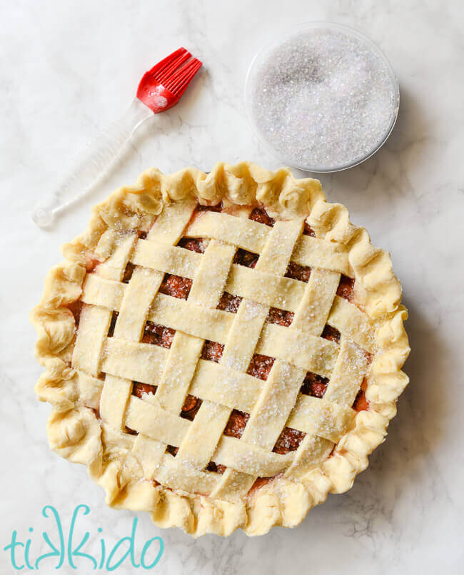 Unbaked cherry pie being brushed with water and sprinkled with sugar crystals.