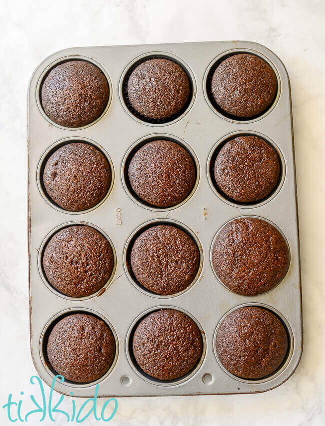 A dozen chocolate crazy cake cupcakes in a cupcake tin on a white marble background