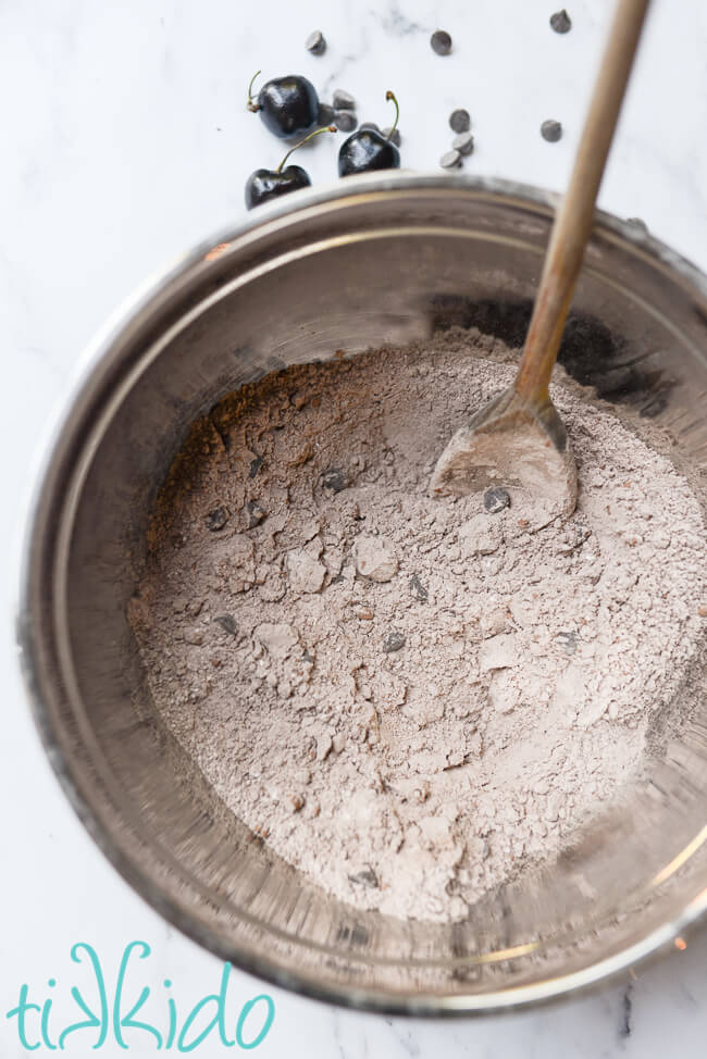 Dry ingredients for chocolate cherry muffins being mixed in a silver bowl.