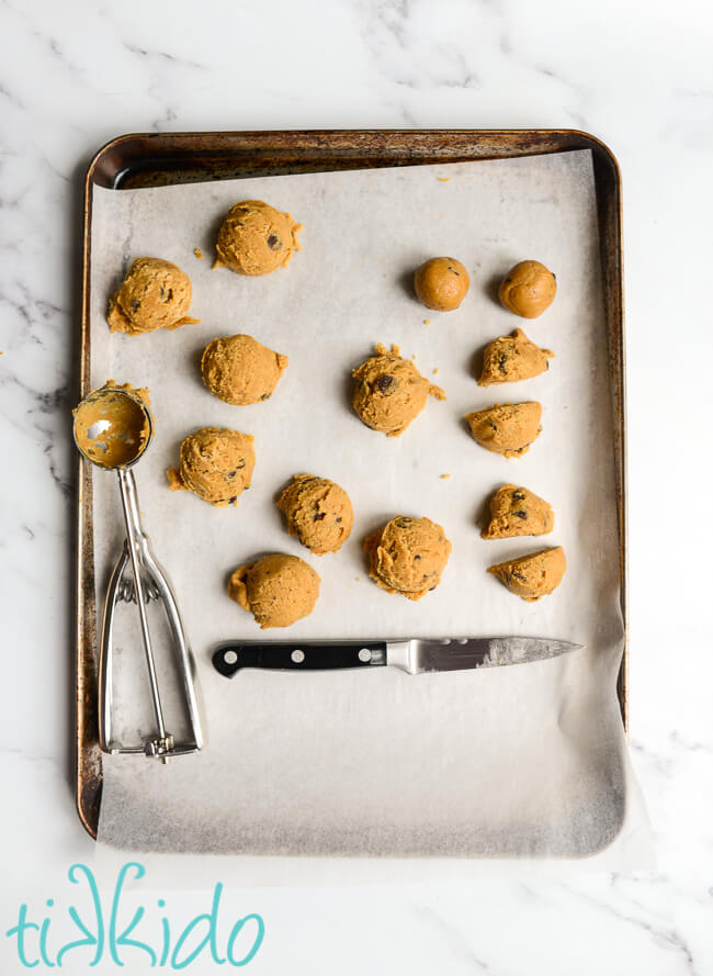 Edible Chocolate Chip Cookie Dough being shaped into bite-sized balls on a parchment lined baking sheet.