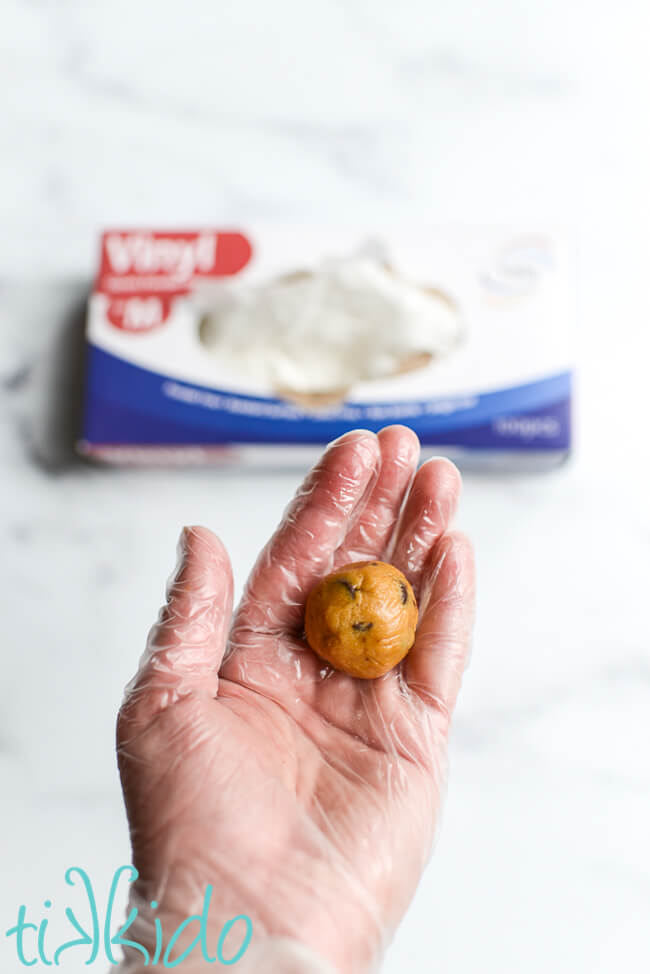 Gloved hand shaping edible cookie dough into balls to make Chocolate Chip Cookie Dough Truffles.