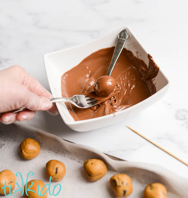 Chocolate Chip Cookie Dough Truffles being dipped in melted milk chocolate.