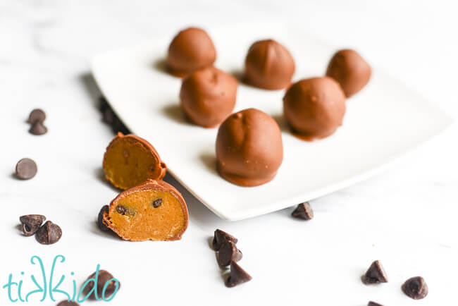 Chocolate chip cookie dough truffles on a white plate, with one truffle cut in half to show the edible cookie dough inside.