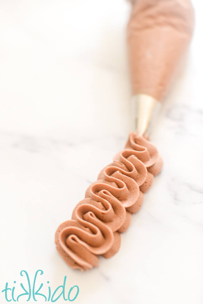 Ruffles of chocolate frosting piped with a star tip on a white marble surface.