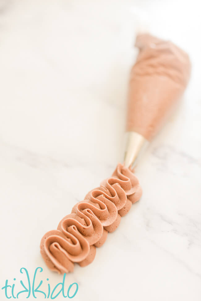 Swirls of chocolate frosting piped out of piping bag with a star tip, on a white marble surface.