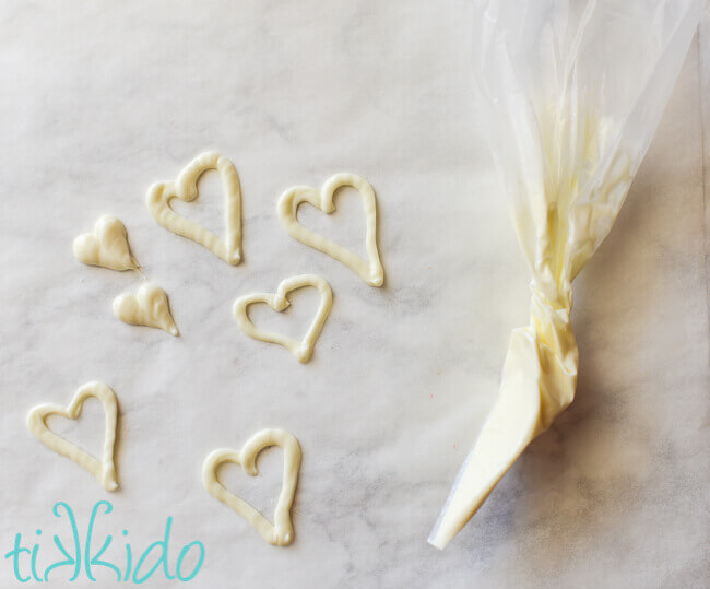white chocolate being piped into heart shapes to make Valentine's day cupcake toppers.