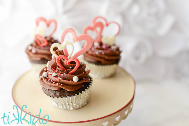 Three cupcakes for Valentine's day decorated with pink and white chocolate hearts.
