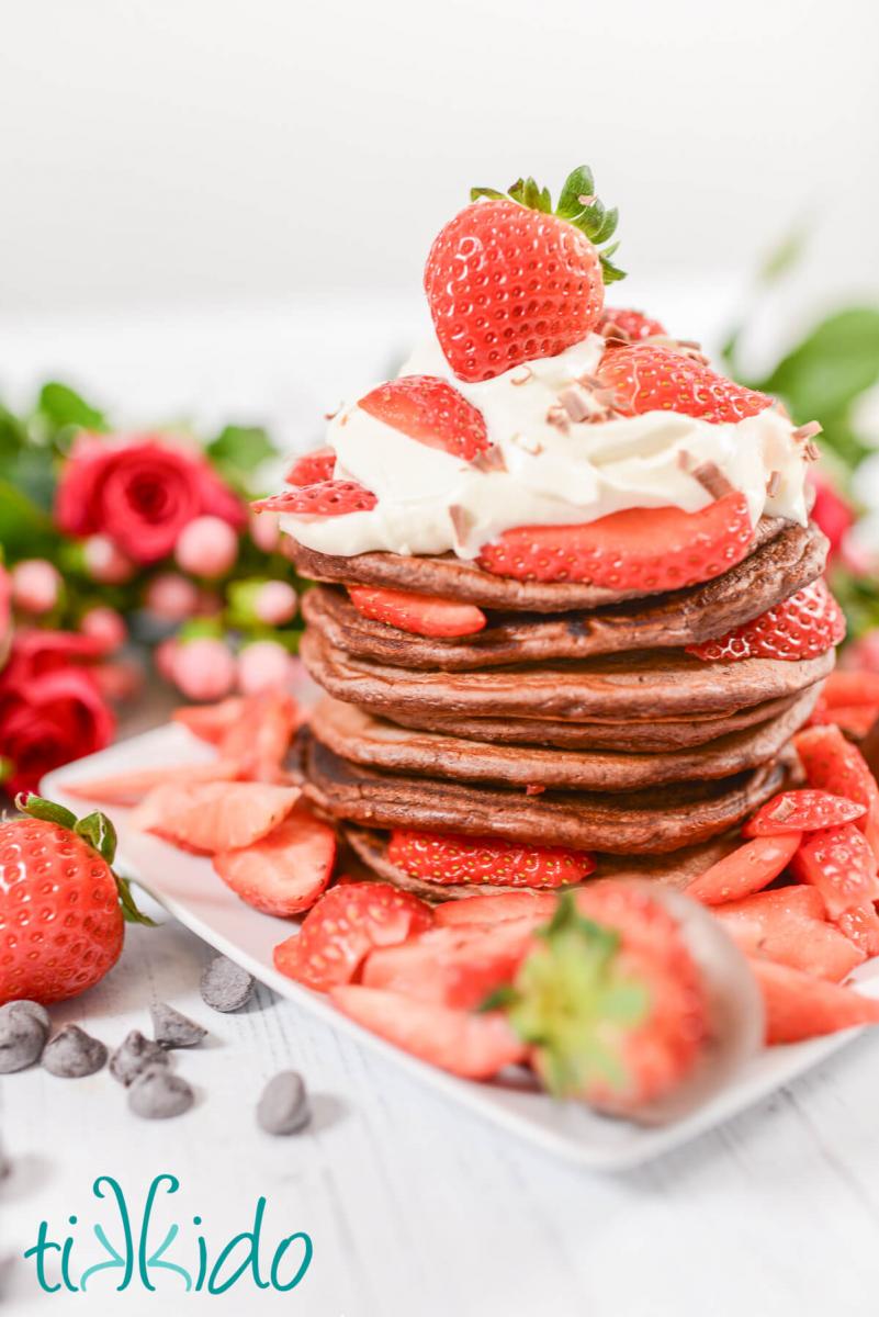 Stack of chocolate pancakes topped with whipped cream, fresh strawberries, and chocolate curls.