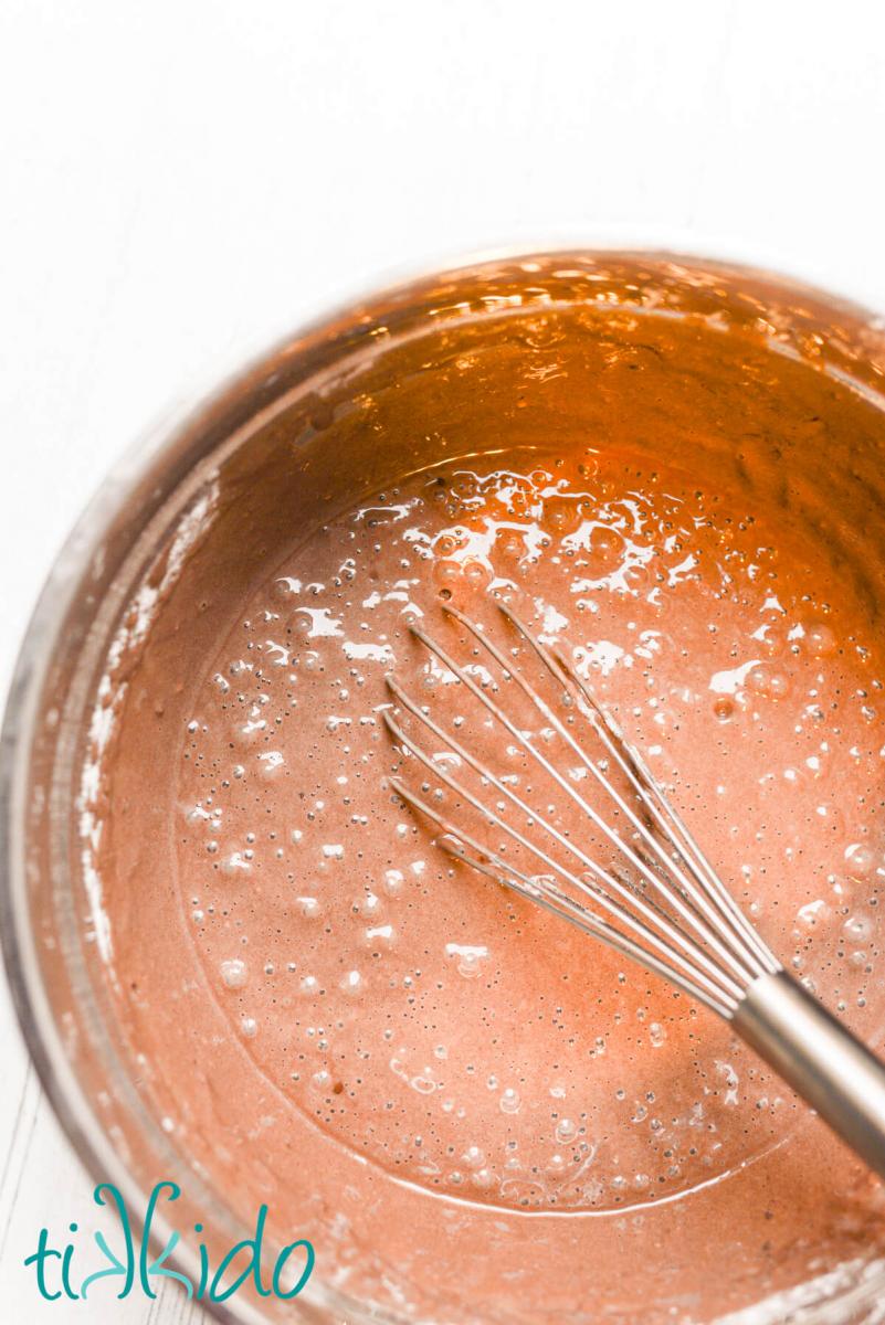 Chocolate pancake batter in a silver bowl with a whisk.