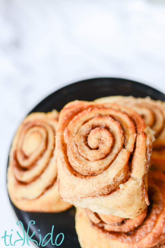 No Knead cinnamon rolls stacked on a black cake plate.