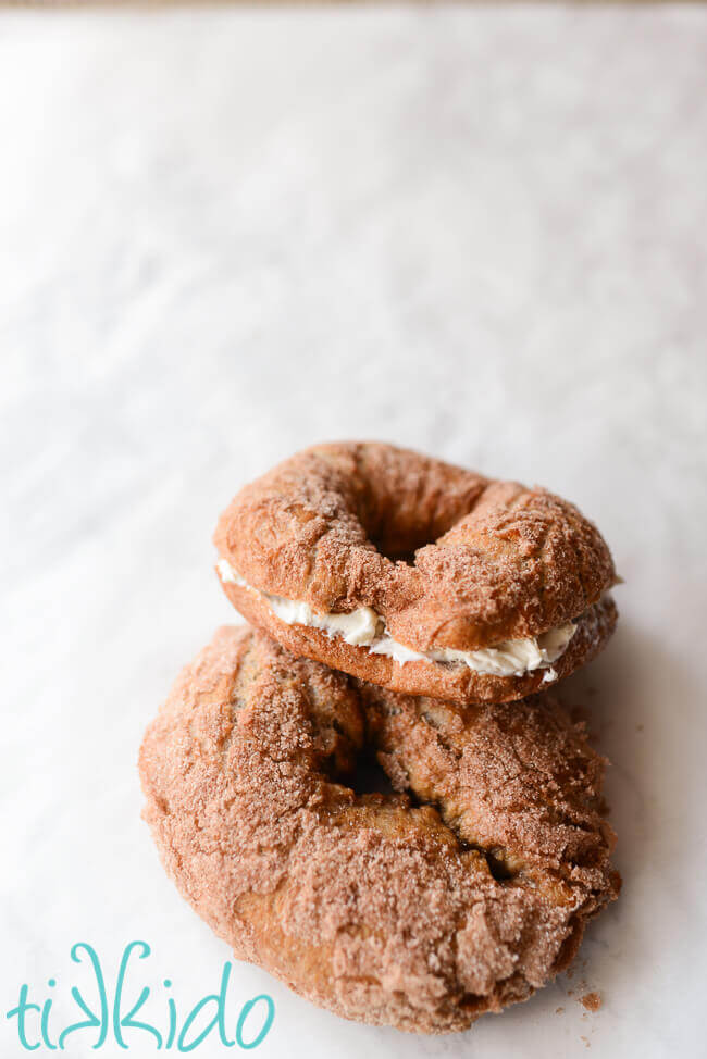 Cinnamon sugar bagels with a cinnamon sugar coating on a white surface, one cut in half and coated with cream cheese.