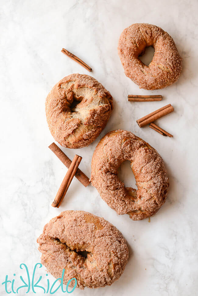 Cinnamon sugar bagels on a white surface surrounded by cinnamon sticks.