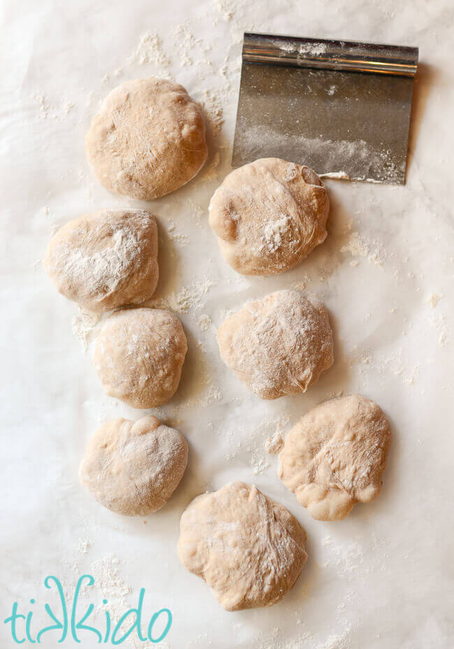 Cinnamon bagel dough shaped into eight disks of dough on a white marble surface.