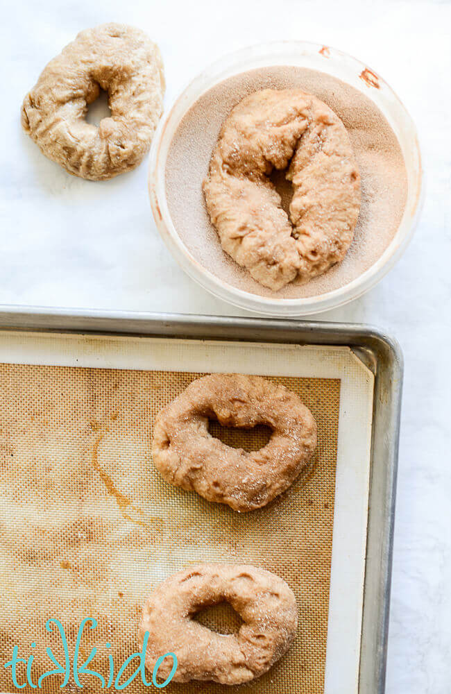 Unbaked cinnamon sugar bagels being coated in cinnamon sugar.