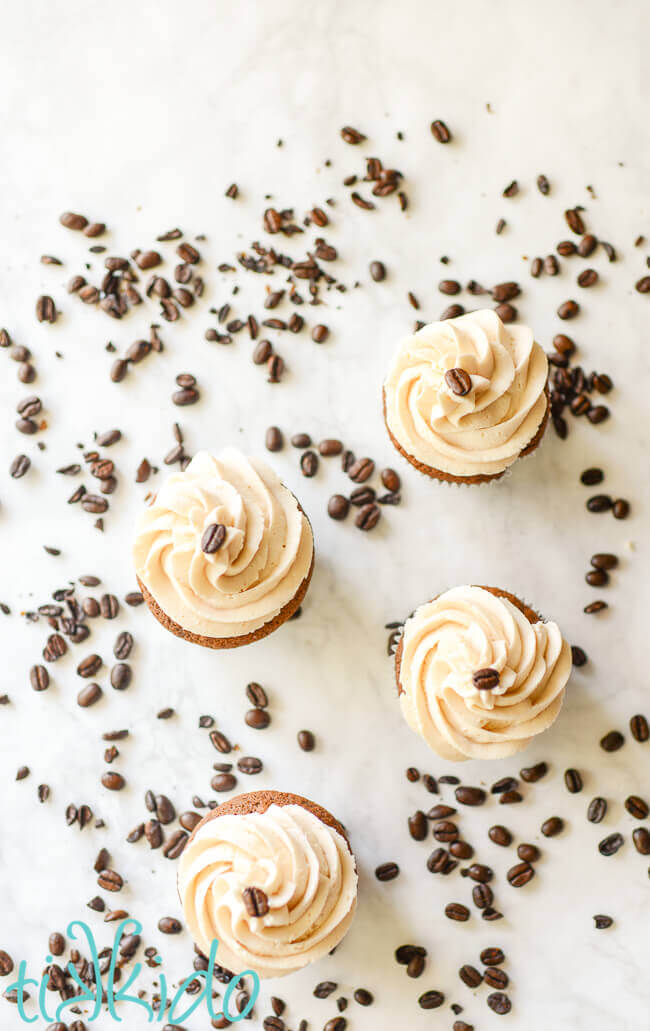 Bailey's frosting swirled on four Irish coffee cupcakes, topped by coffee beans and surrounded by scattered coffee beans.