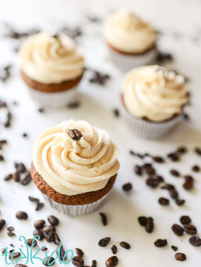 Four coffee cupcakes topped with Bailey's frosting on a white background, surrounded by coffee beans.