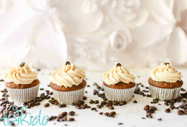 Four coffee cupcakes topped with Bailey's frosting on a white background, surrounded by coffee beans.