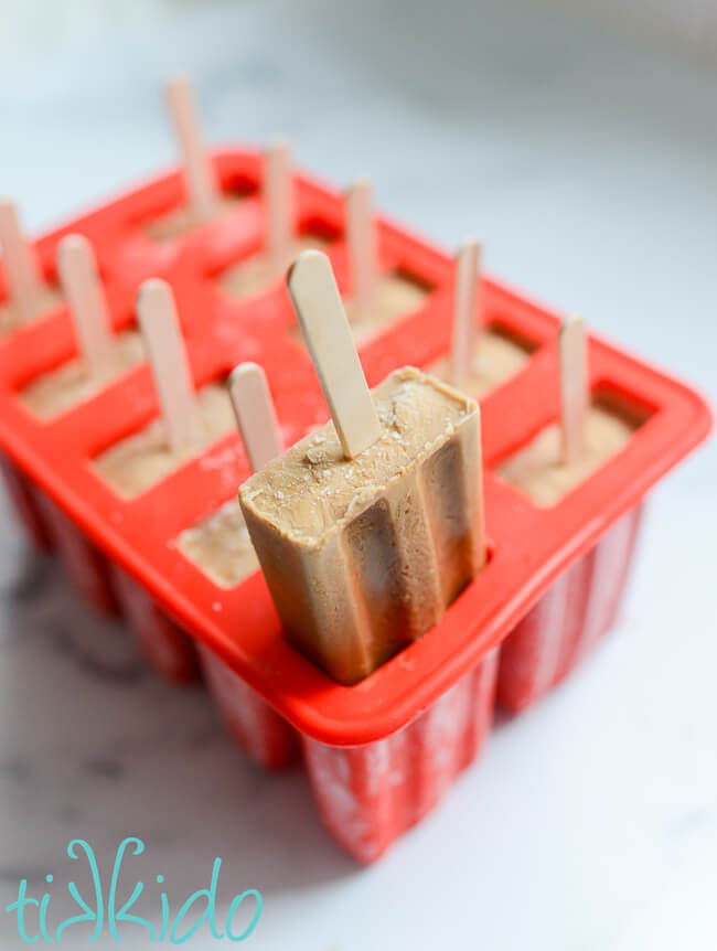 A coffee popsicle halfway pulled out of a red silicone popsicle mold.