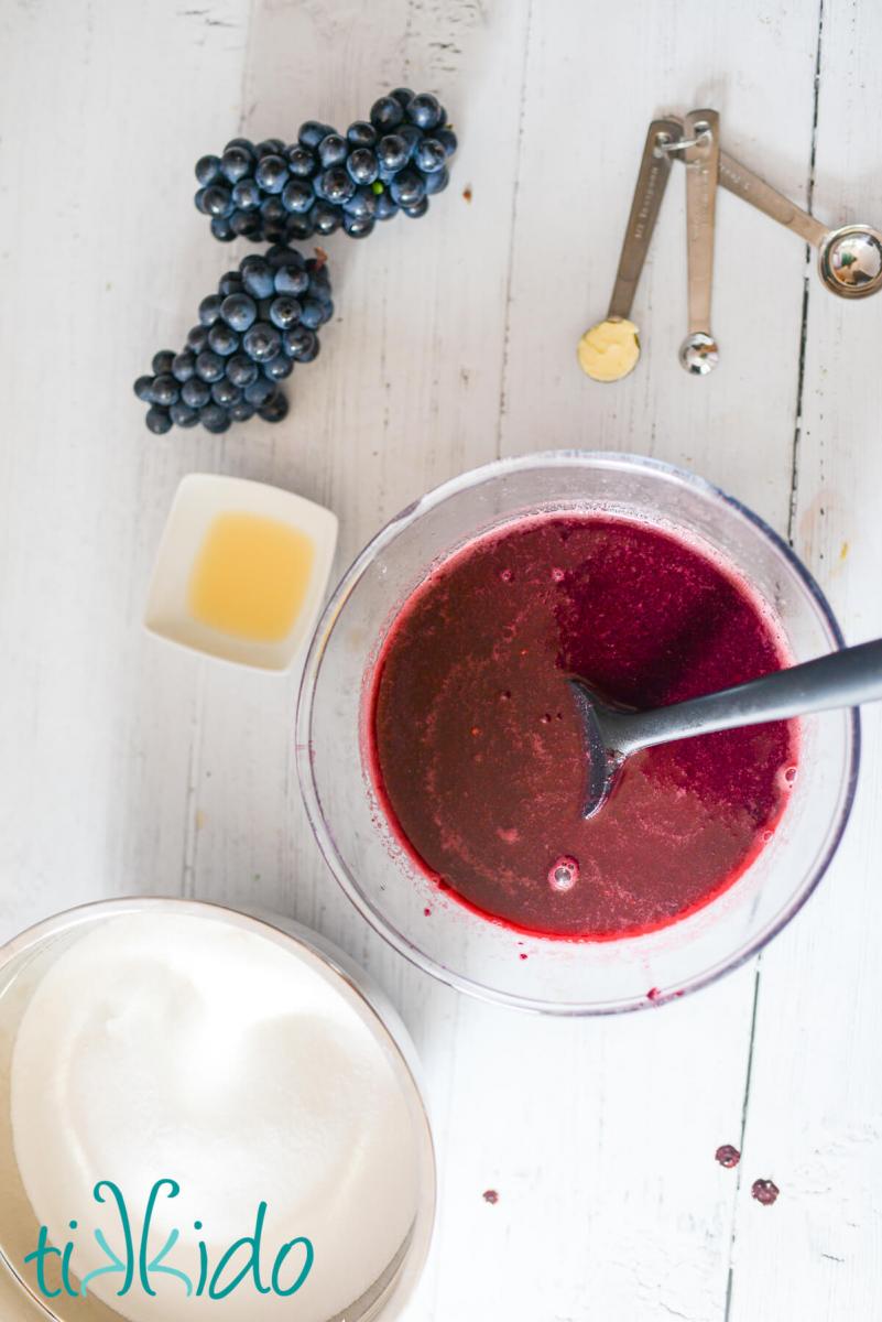 Ingredients for homemade concord grape jam recipe on a white wooden surface.