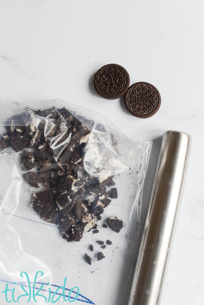 Oreo cookies being crushed with a silver rolling pin to make Cookies and Cream Cereal Treats.