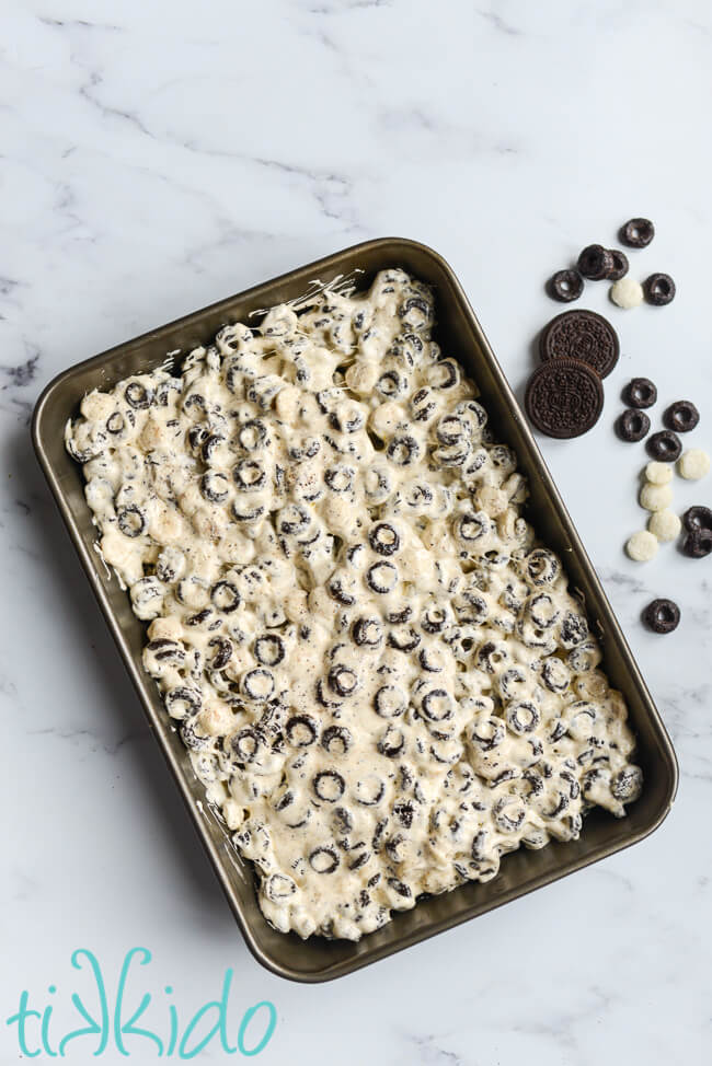 Cookies and Cream Cereal Treats cooling in a 9x13 pan on a marble surface.