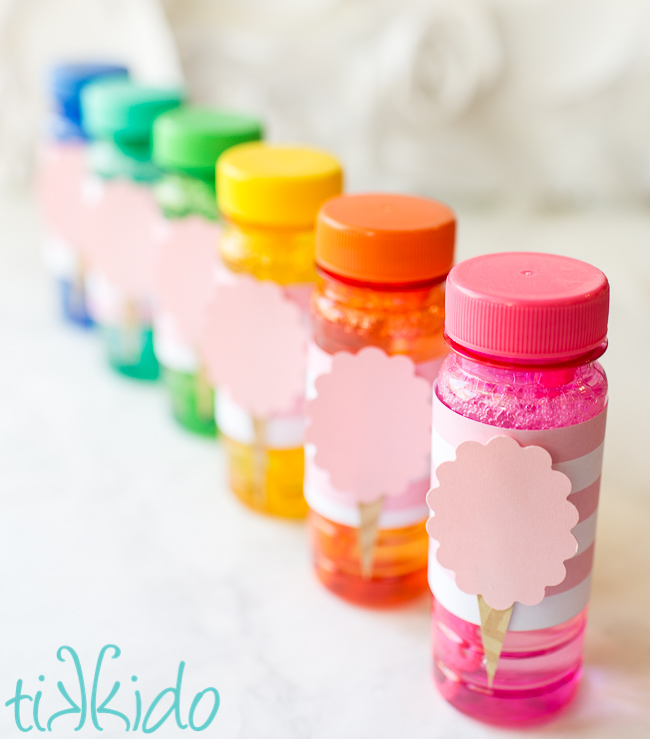 Bottles of customized bubbles favors decorated for a cotton candy birthday party, lined up in rainbow color order.