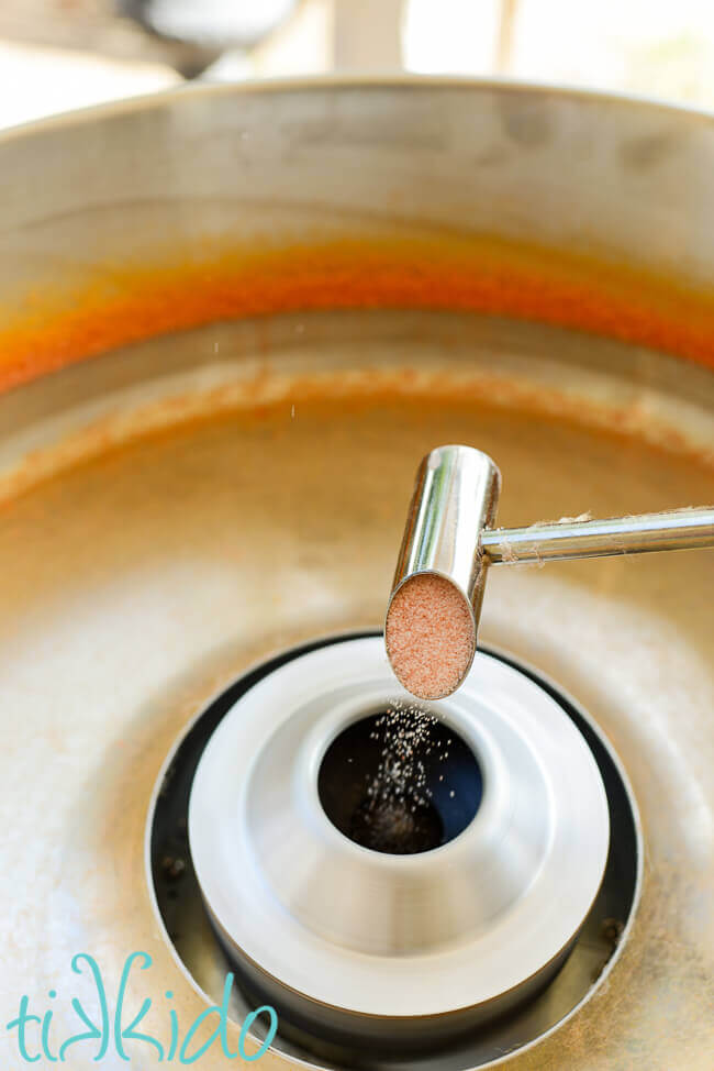 Orange cotton candy sugar being poured into the center of a cotton candy machine.