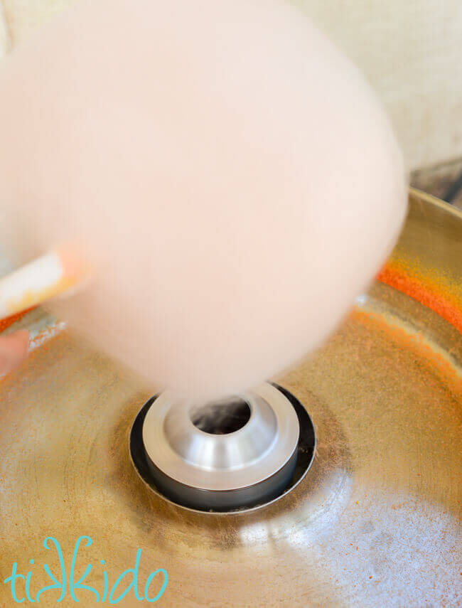 Orange cotton candy being spun in a cotton candy machine.