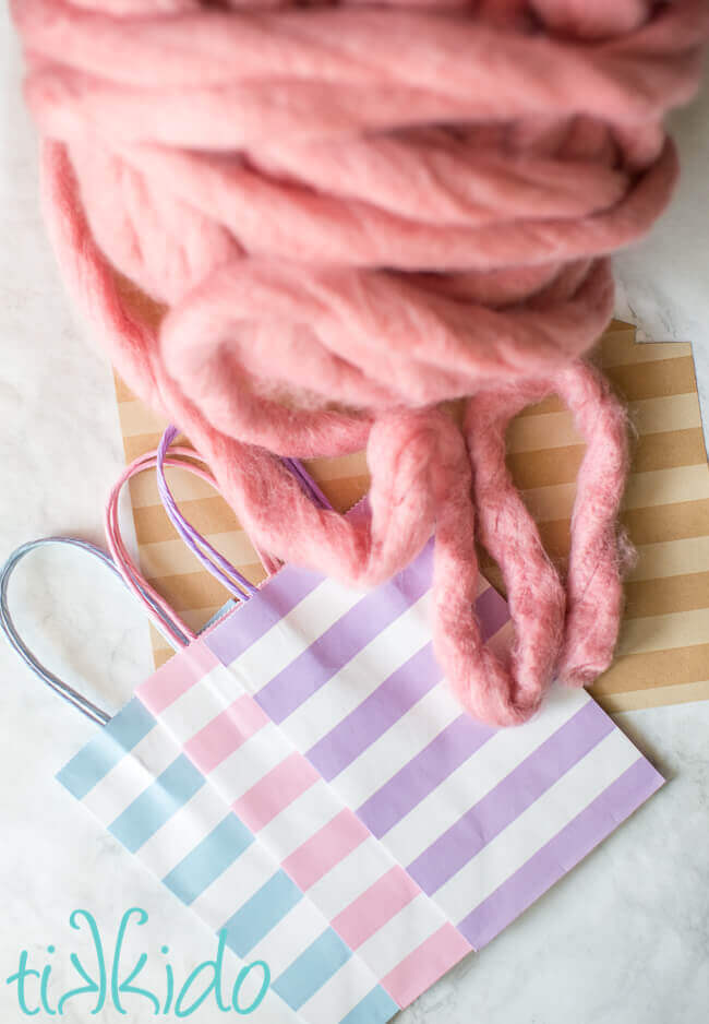 Chunky pink roving yarn, scrapbook paper, and pastel striped gift bags for making cotton candy party favor bags.