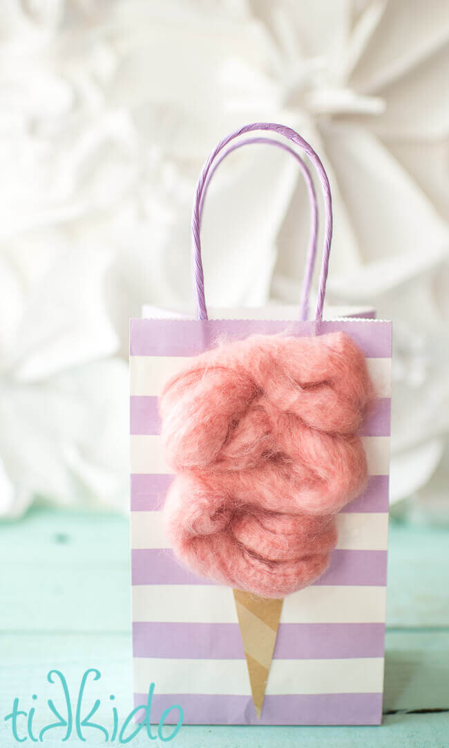 Purple striped gift bag decorated with a fluffy pink cotton candy decoration to make cotton candy party favors.