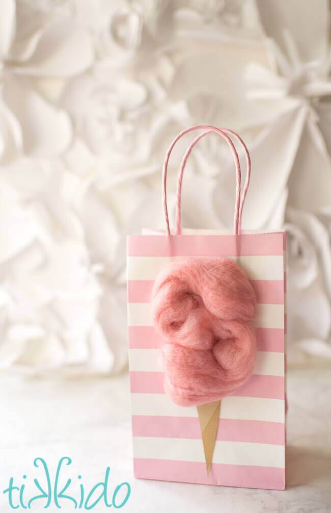 Pink striped gift bag decorated with a fluffy pink cotton candy decoration to make cotton candy party favors.