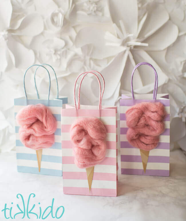 Three cotton candy party favor bags with fluffy pink cotton candy decorations on a marble background.
