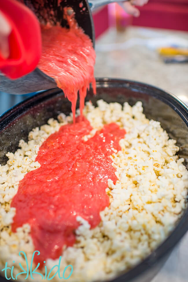 Hot sugar mixture being poured over popcorn to make cotton candy popcorn.