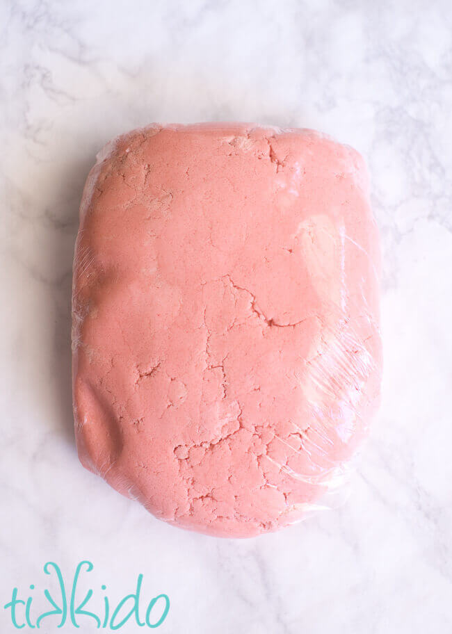 Cotton candy cookie dough wrapped in plastic cling wrap on a white marble table.